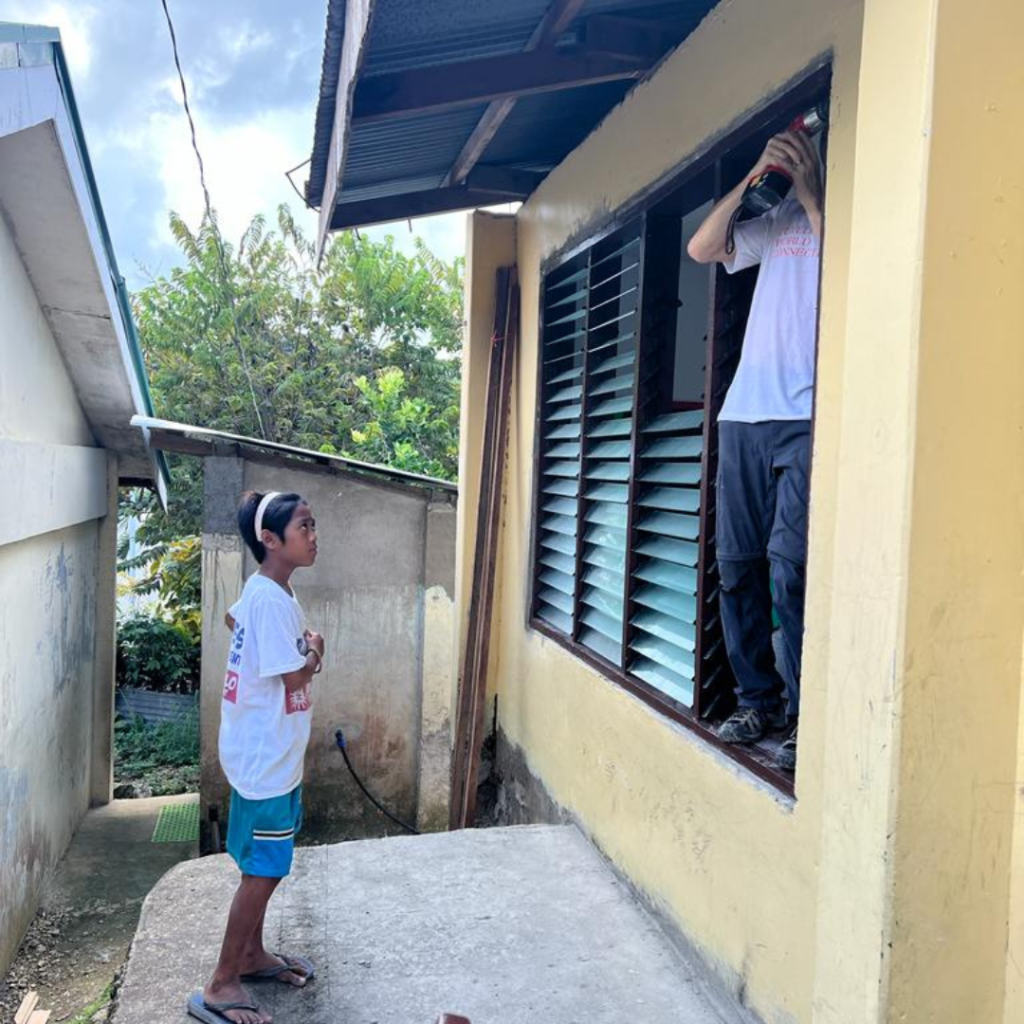 Volunteer standing in window seal with local child looking on Philippines