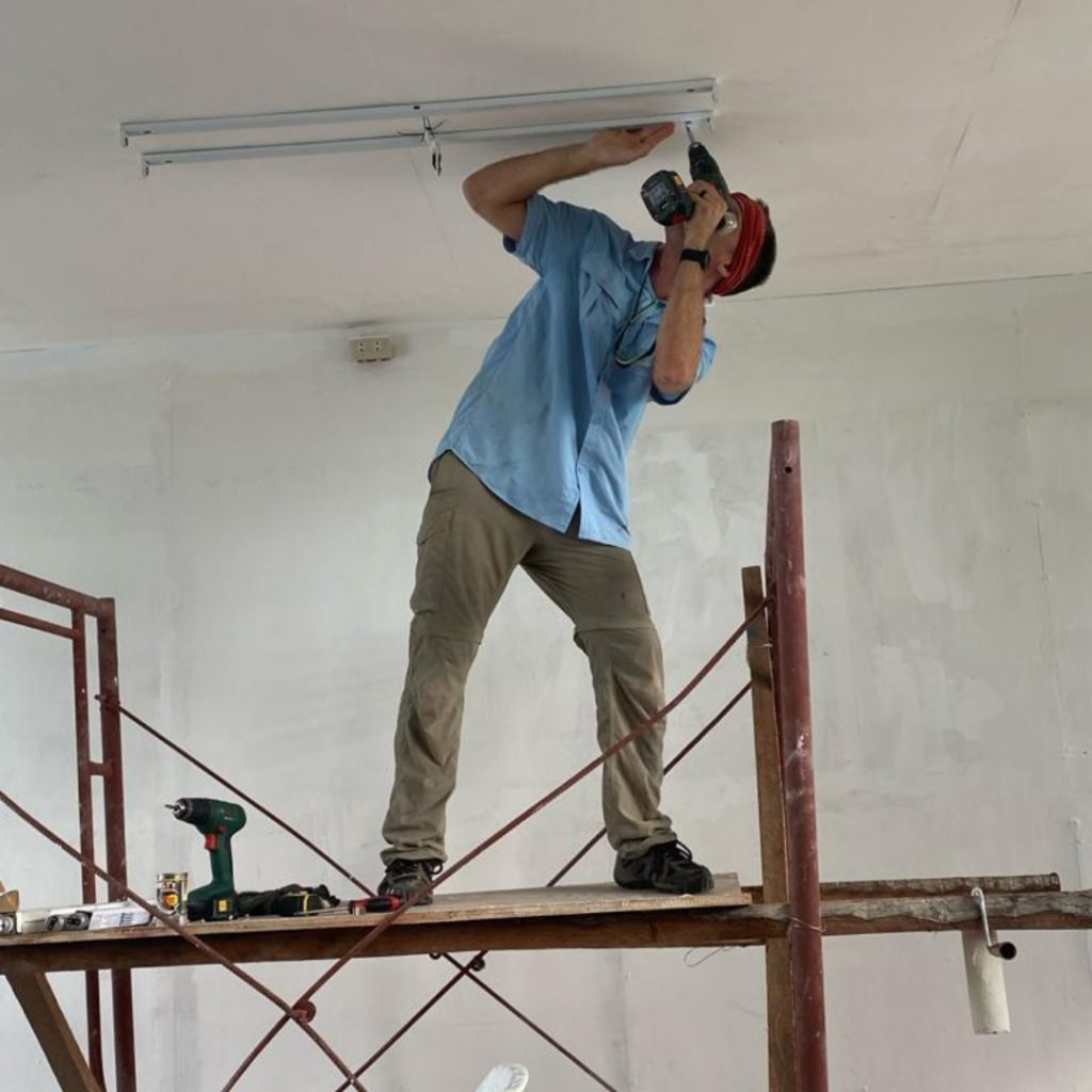 Volunteer installing ceiling light fixture in school classroom Philippines
