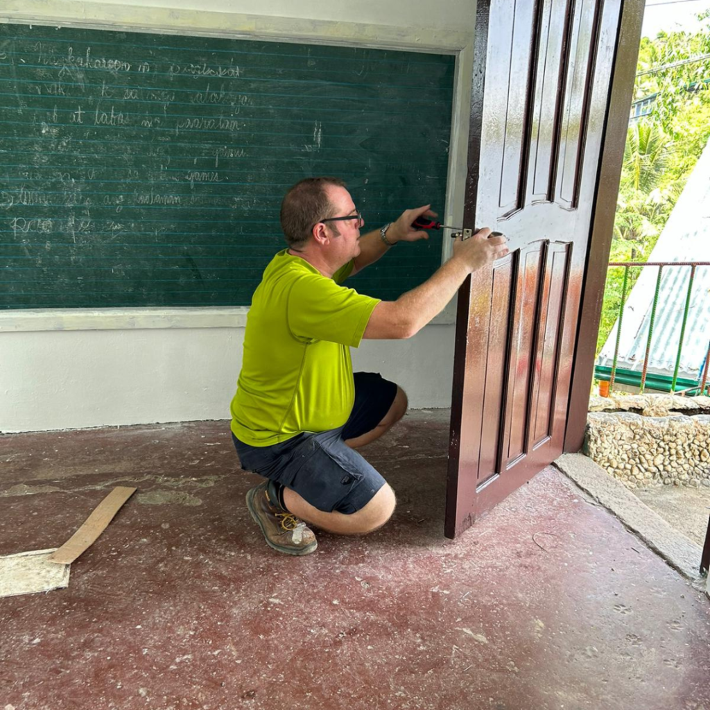 Volunteer repairing doorhandle of classroom door Philippines