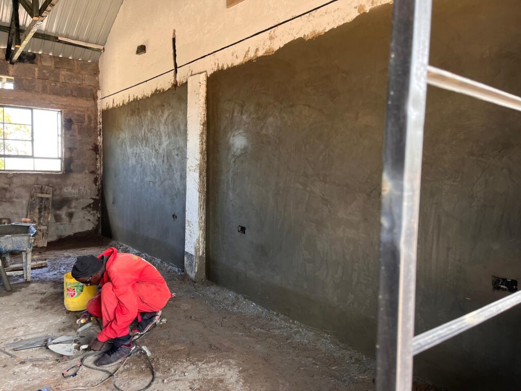 Local worker smoothing mud walls at project site Kenya