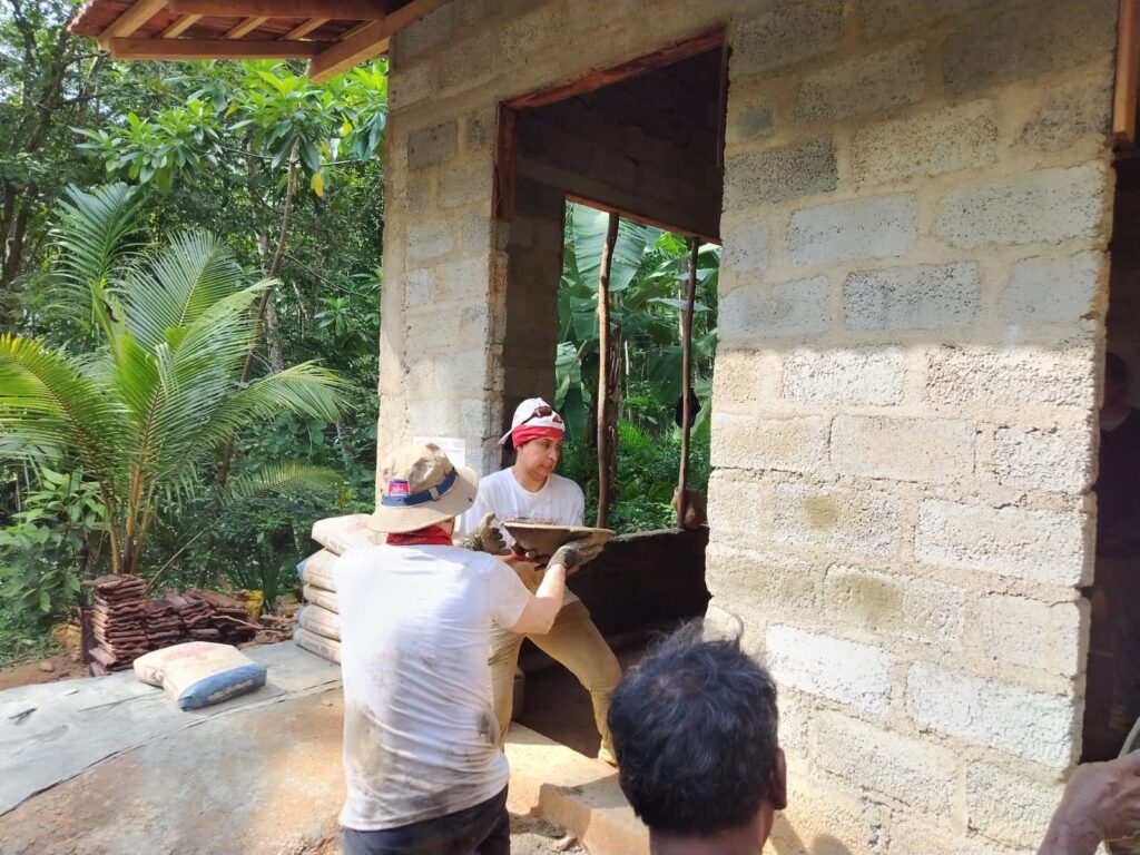 Volunteers passing bowl of cement through doorway of project site Sri Lanka