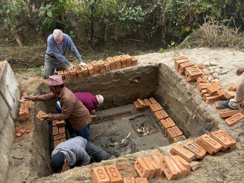 Volunteers and local tradespeople in pit working with bricks Nepal